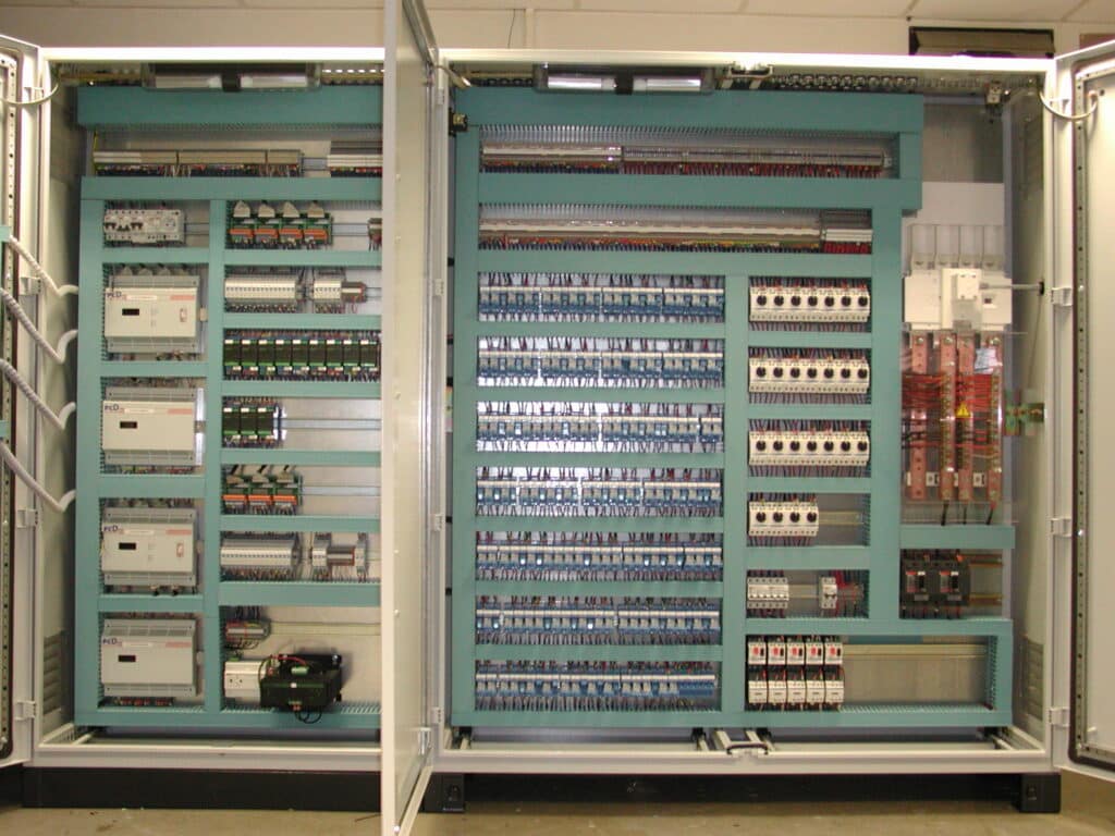 Armoires Électriques Industrielles | Installation PLC Intérieur d'une armoire électrique industrielle ouverte, avec PLCs 'pCD', câblage complexe, disjoncteurs et borniers.