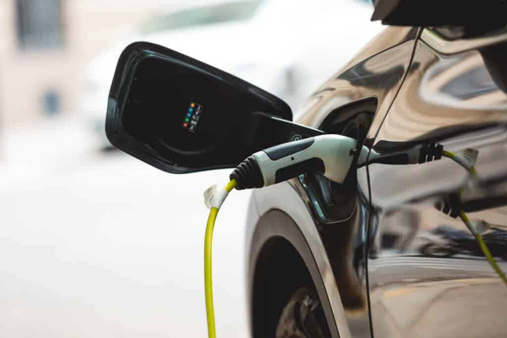 Voiture électrique noire en charge. Un câble vert vif est branché, montrant les voyants du port et l'étiquette '35088803 TPV-EV-102.394A'.