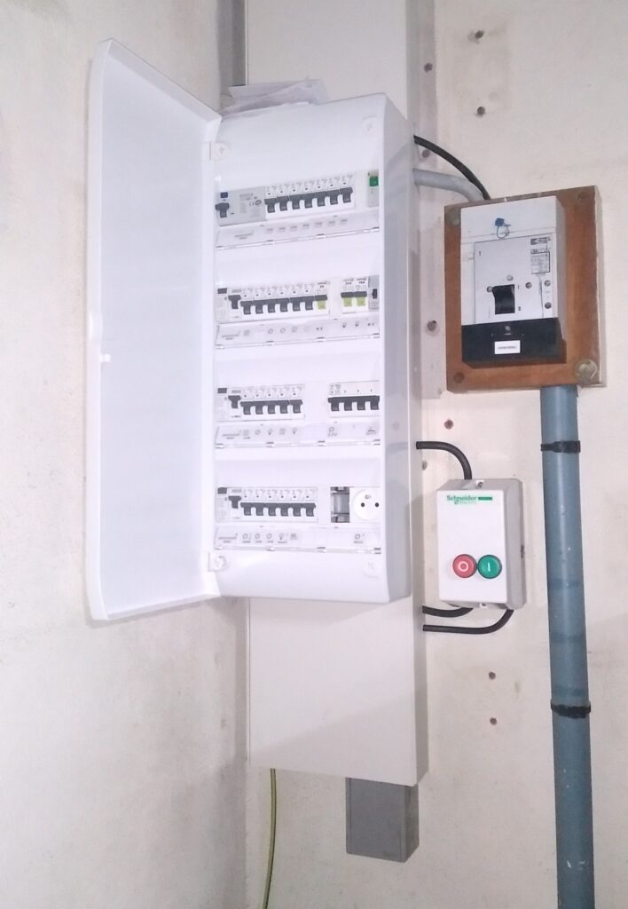 Tableau électrique ouvert avec disjoncteurs et boîtier de commande Schneider Electric avec boutons marche-arrêt.